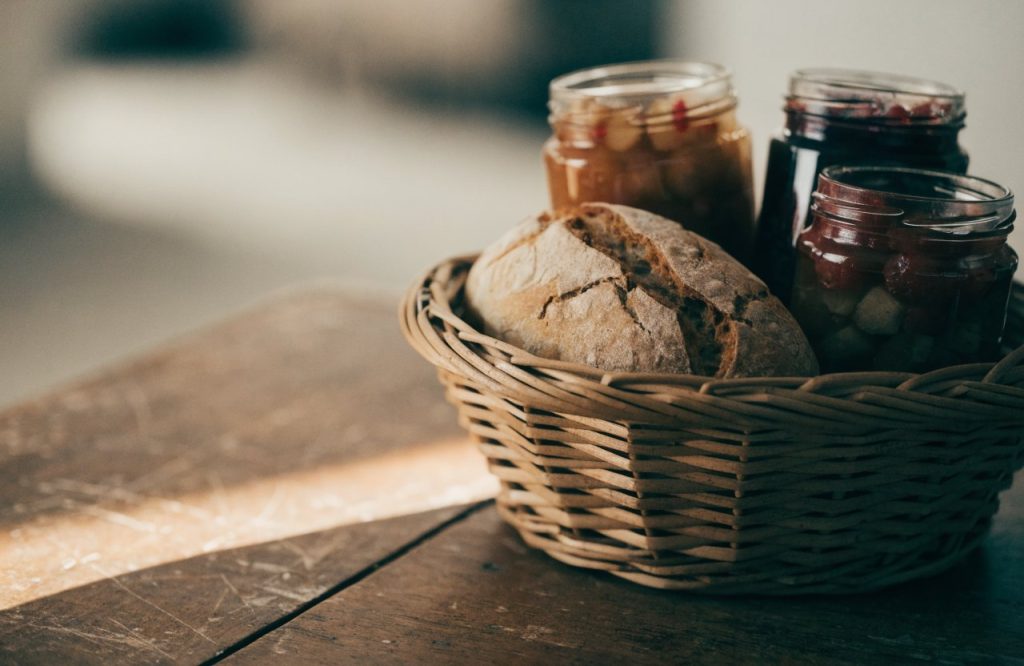 Immagine illustrativa di un cesto di vimini con conserve e pane — non raffigura il luogo
